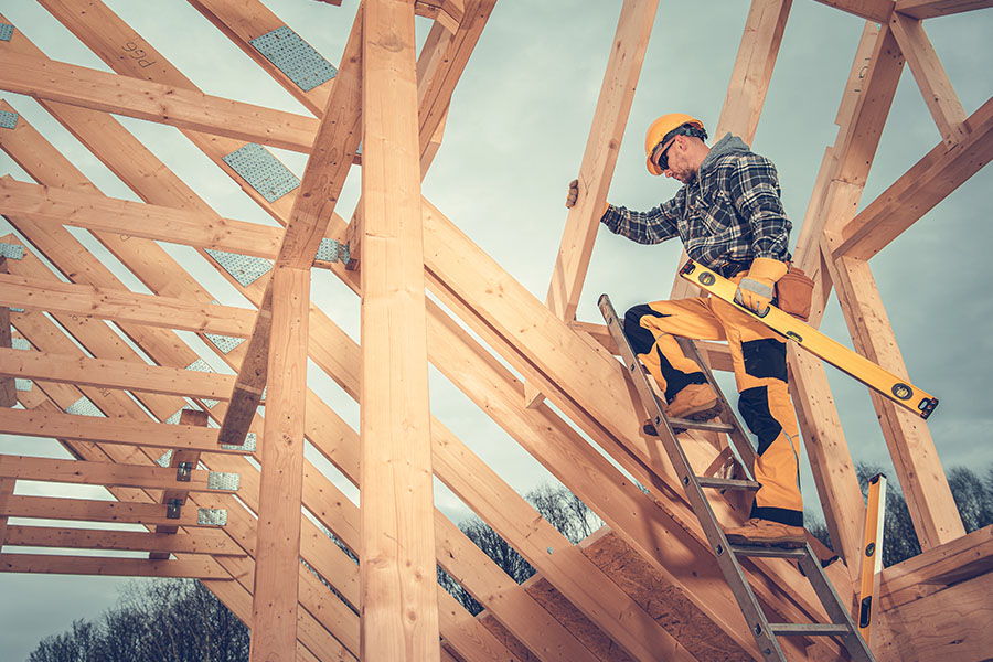 Specialized Business Insurance - View of Construction Worker Holding a Level and Working on the Frame of a House While Standing on a Ladder