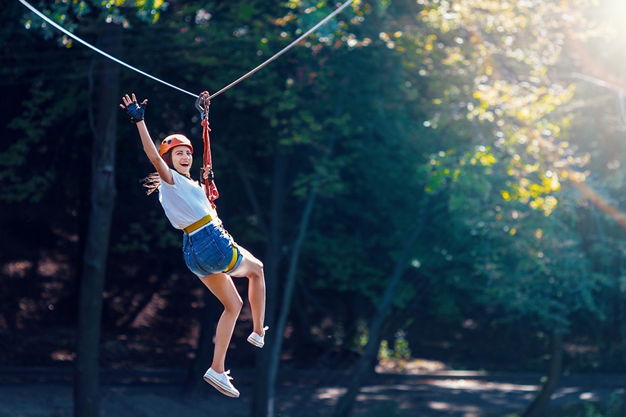 Adventure-and-Entertainment-Insurance-Cheerful-Woman-Waves-as-She-is-Gliding-Along-a-Zipline-in-an-Adventure-Park